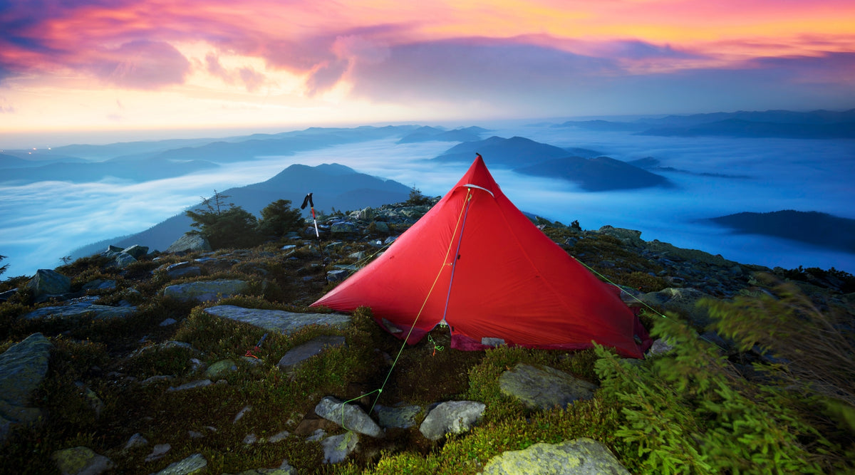Tente pyramide rouge au sommet d'une montagne avec ciel nuageux