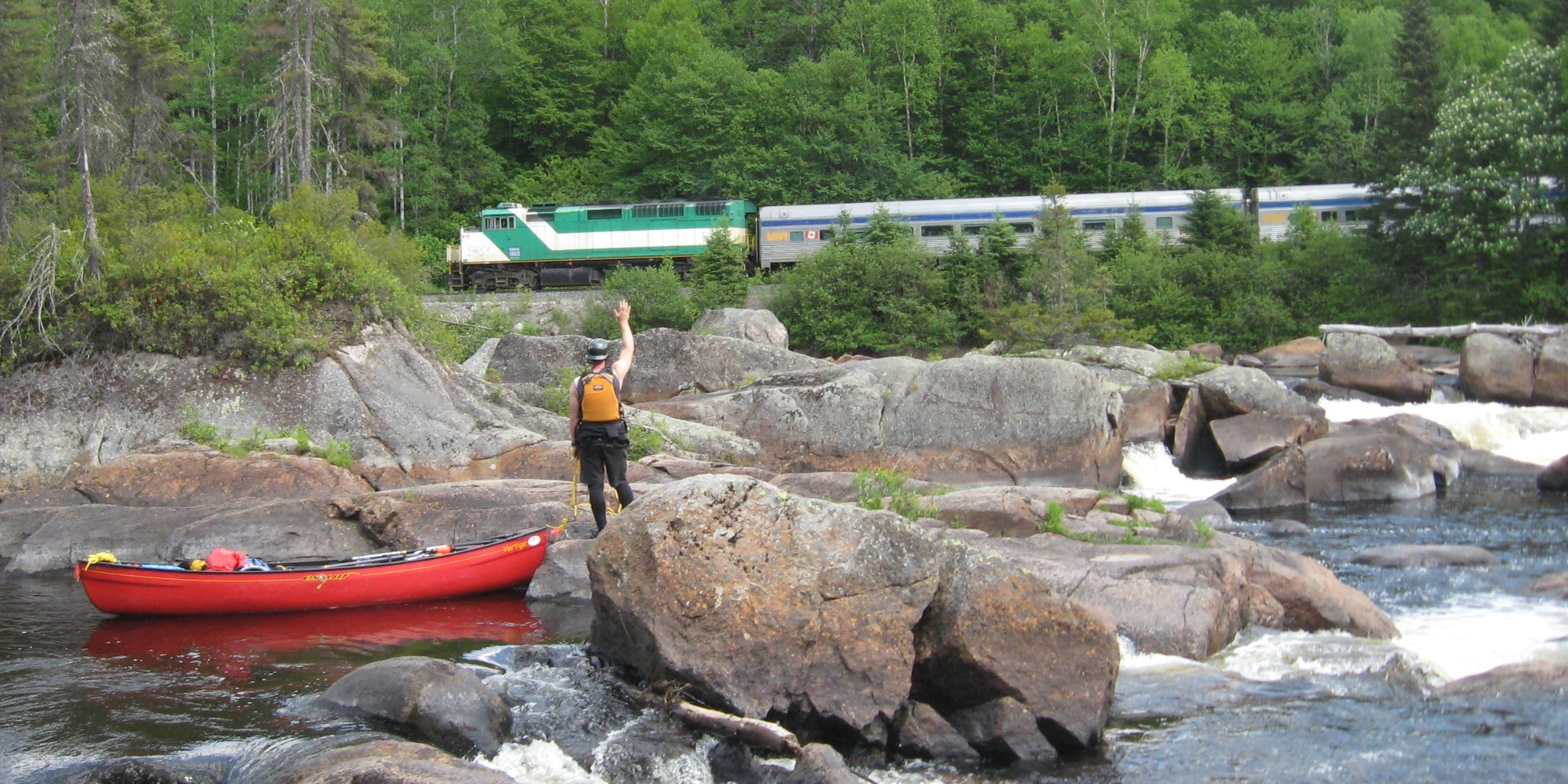 Expédition en canot sur  la rivière Batiscan - Un canoteur en cordelle dans un rapide salue un train Via Rail