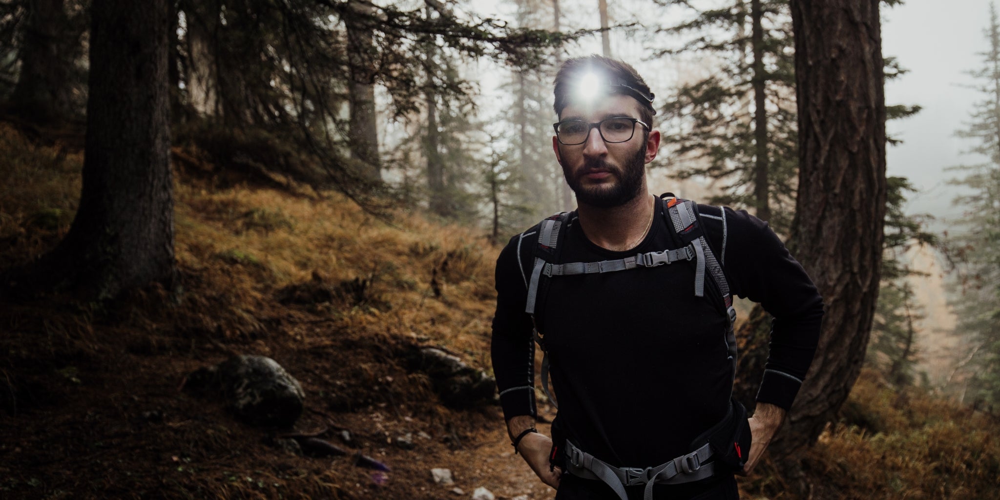 Randonneur dans un sentier en forêt avec lampe frontale et sac à dos 