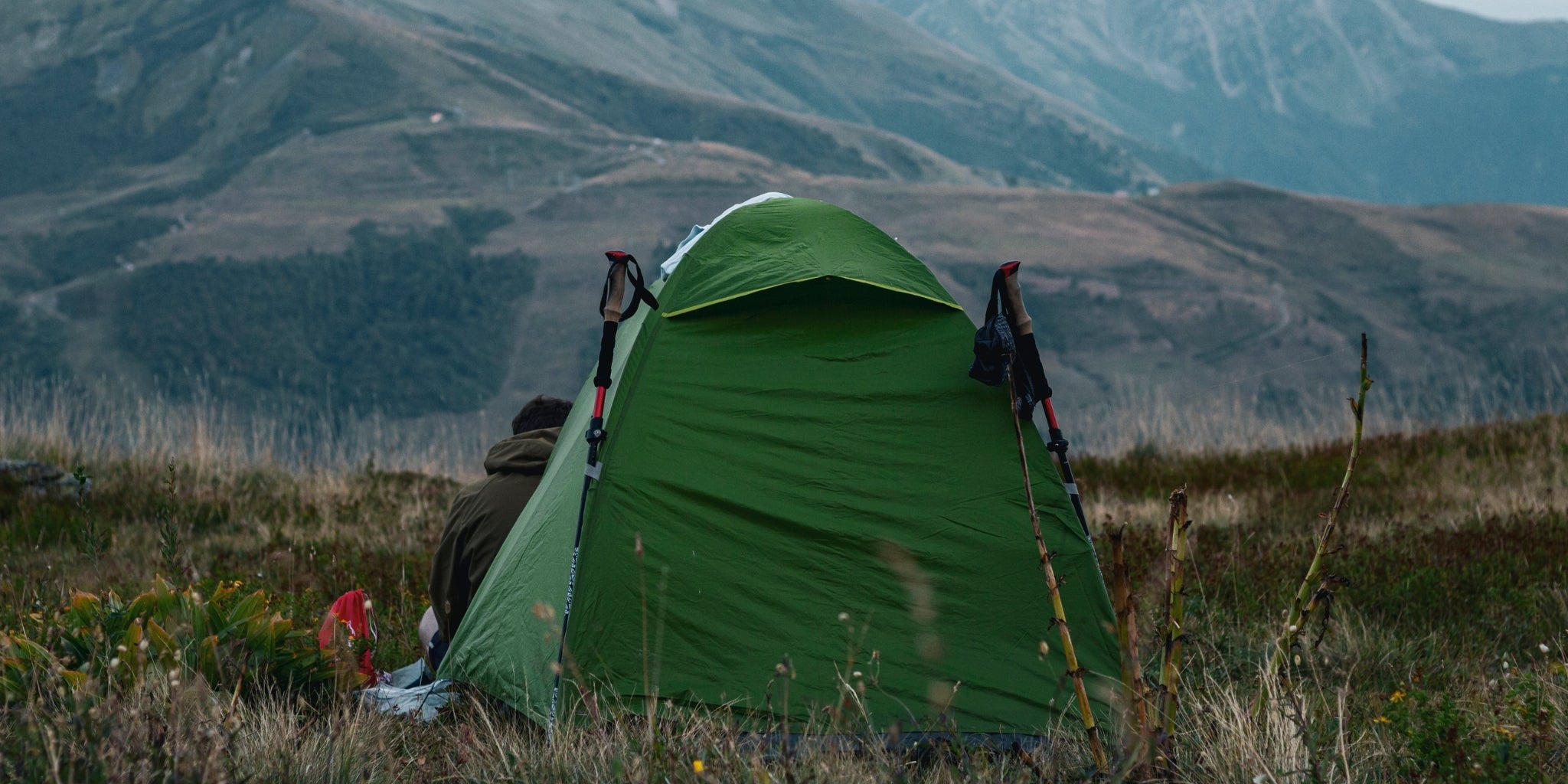 Randonneur solitaire assis devant sa tente autoportante 1 place - Tente dôme verte face aux montagnes